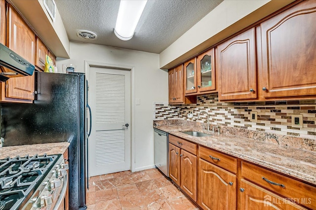 kitchen featuring brown cabinets, visible vents, appliances with stainless steel finishes, a sink, and light stone countertops