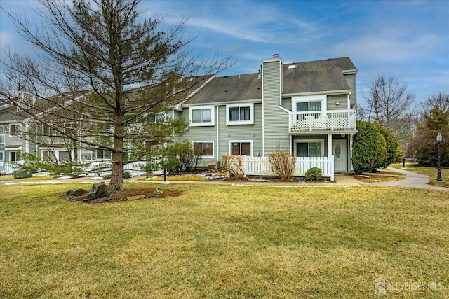 back of property with a balcony, a chimney, and a yard