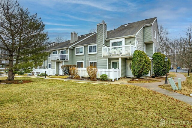 rear view of property featuring a lawn and a balcony