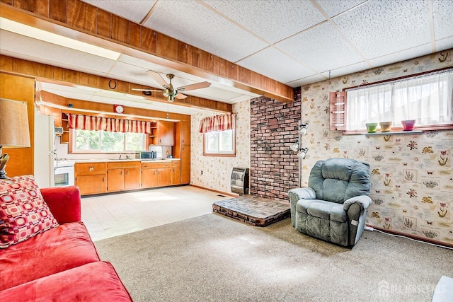living room with a drop ceiling, ceiling fan, wallpapered walls, light carpet, and baseboards