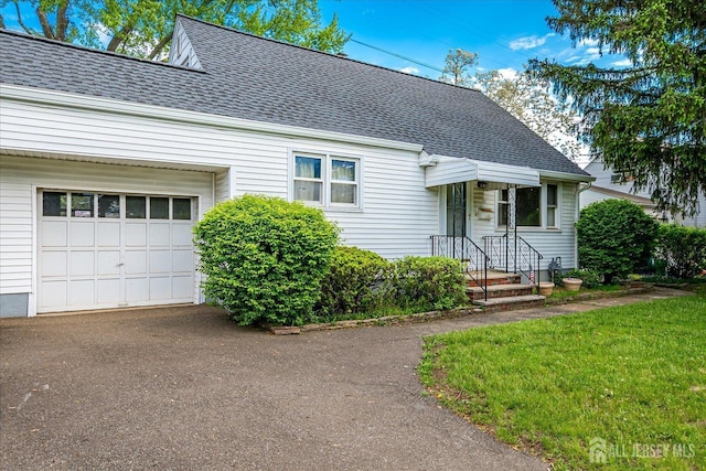 view of front facade featuring roof with shingles, an attached garage, asphalt driveway, and a front lawn