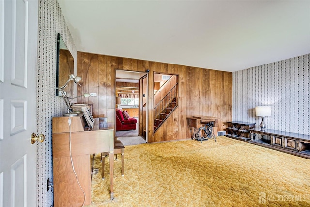 carpeted living area with stairs and wooden walls