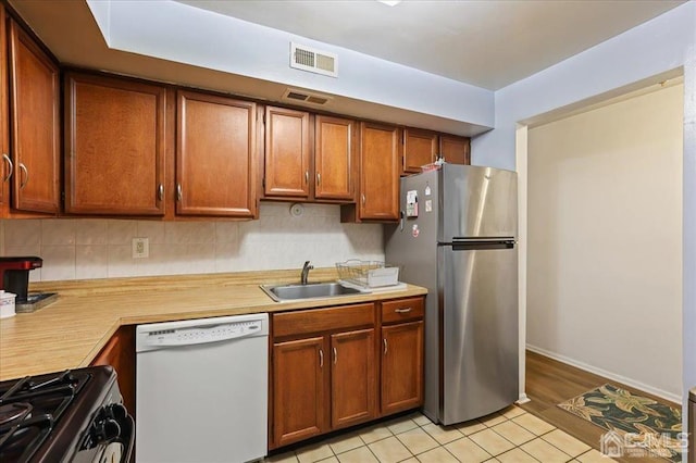 kitchen with light hardwood / wood-style flooring, stainless steel fridge, white dishwasher, sink, and decorative backsplash