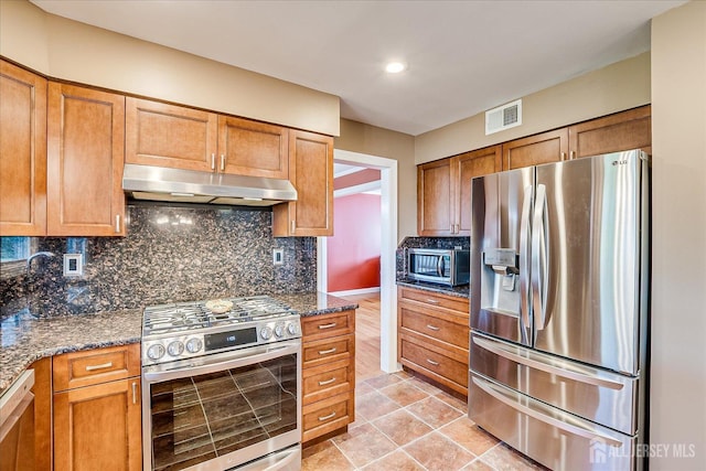 kitchen with tasteful backsplash, under cabinet range hood, visible vents, brown cabinetry, and stainless steel appliances