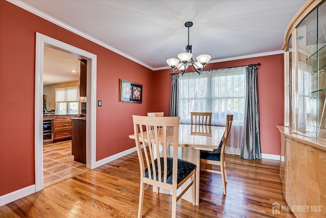 dining area with light wood finished floors, an inviting chandelier, wine cooler, ornamental molding, and baseboards