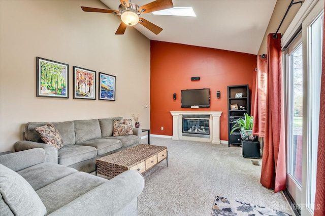 living room featuring high vaulted ceiling, ceiling fan, light colored carpet, a glass covered fireplace, and baseboards
