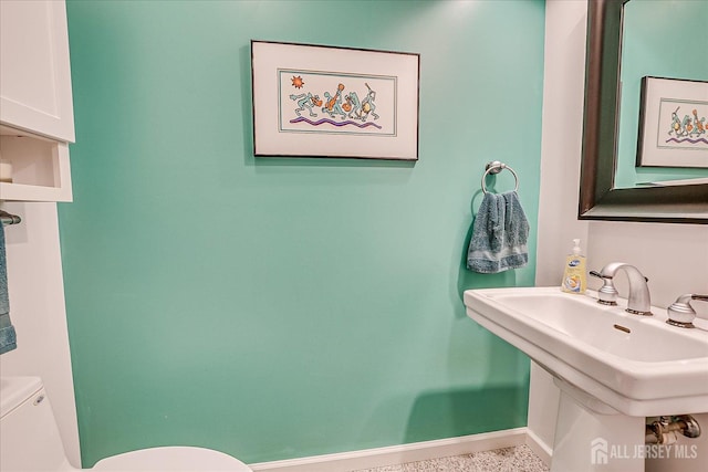 half bathroom featuring toilet, a sink, baseboards, and speckled floor
