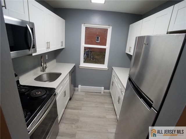 kitchen featuring light wood finished floors, stainless steel appliances, a sink, white cabinetry, and light countertops