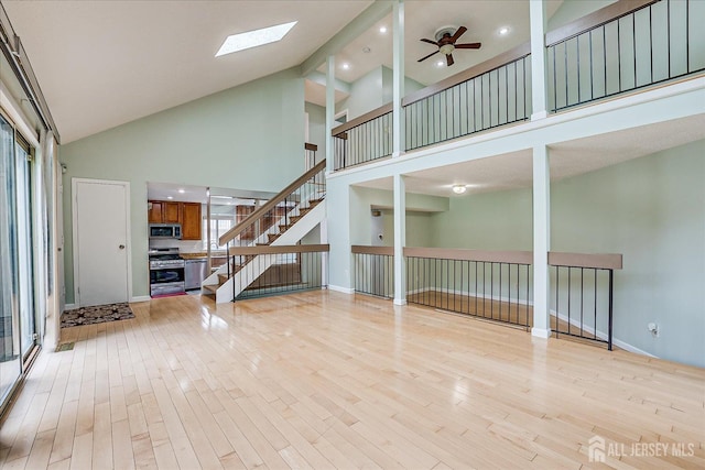 68 Kelly Dr, Edison, NJ 08820 - unfurnished living room with high vaulted ceiling, a skylight, stairway, light wood-style flooring, and a ceiling fan