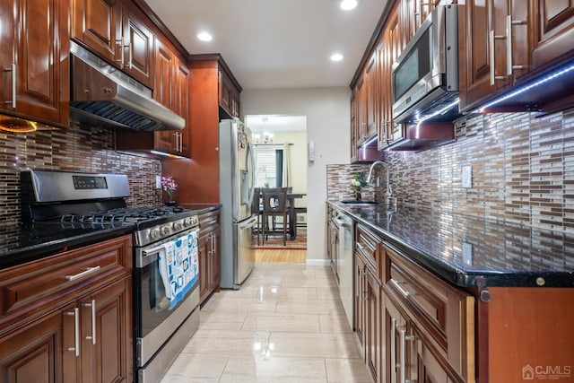 kitchen featuring stainless steel appliances, tasteful backsplash, an inviting chandelier, dark stone countertops, and sink