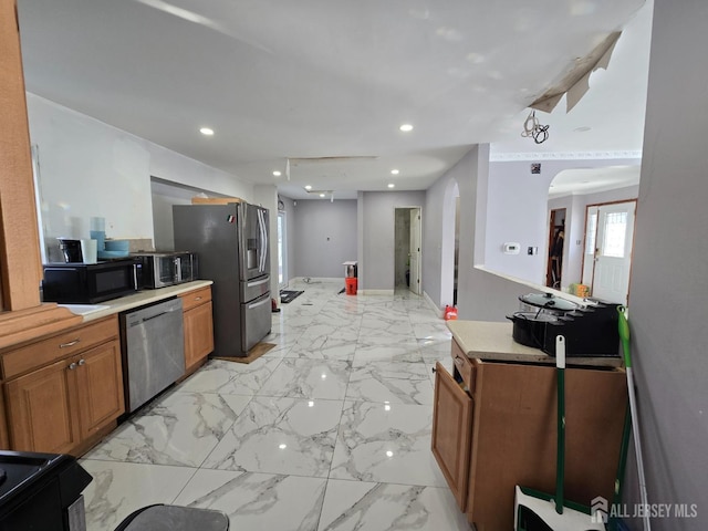 kitchen featuring recessed lighting, arched walkways, appliances with stainless steel finishes, brown cabinetry, and light countertops