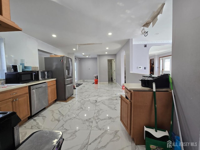 kitchen featuring marble finish floor, appliances with stainless steel finishes, brown cabinetry, and light countertops