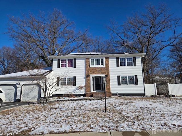 colonial home with solar panels, fence, a garage, and driveway