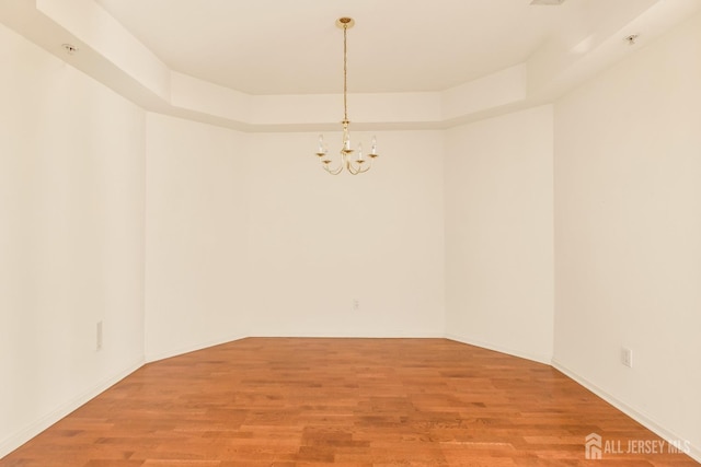unfurnished room with light wood-type flooring, an inviting chandelier, and baseboards