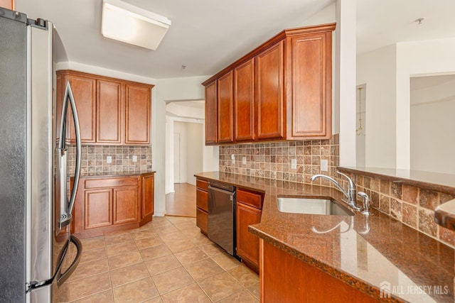 kitchen featuring tasteful backsplash, dark stone countertops, freestanding refrigerator, dishwashing machine, and a sink