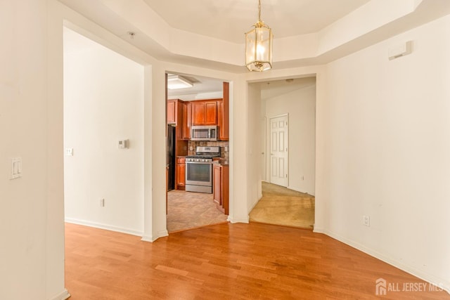 unfurnished room with a tray ceiling, light wood-style flooring, and baseboards