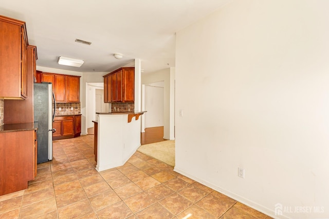 kitchen with a breakfast bar, dark countertops, visible vents, freestanding refrigerator, and decorative backsplash
