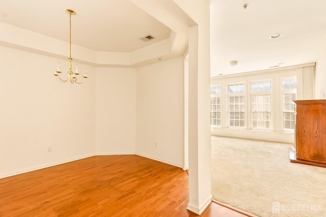 spare room featuring a chandelier, wood finished floors, visible vents, and baseboards