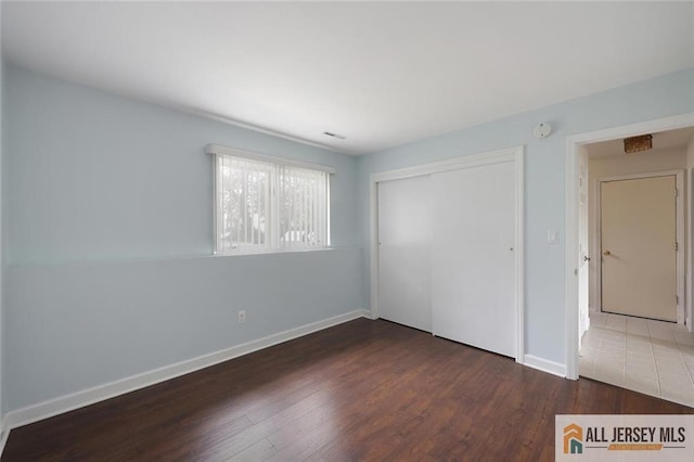 unfurnished bedroom featuring baseboards, a closet, visible vents, and wood finished floors