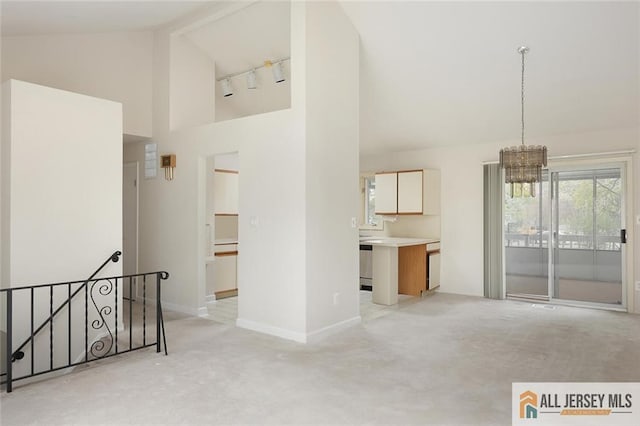 unfurnished living room with baseboards, a notable chandelier, high vaulted ceiling, and light colored carpet