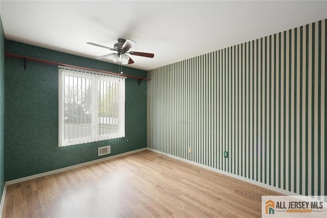 empty room with a ceiling fan, visible vents, wallpapered walls, and wood finished floors