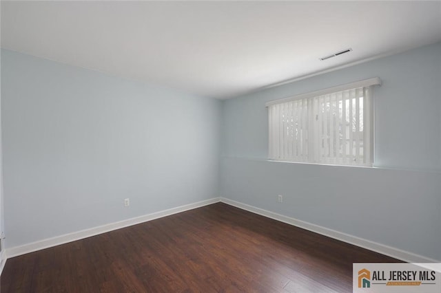 unfurnished room featuring baseboards, dark wood-type flooring, and visible vents