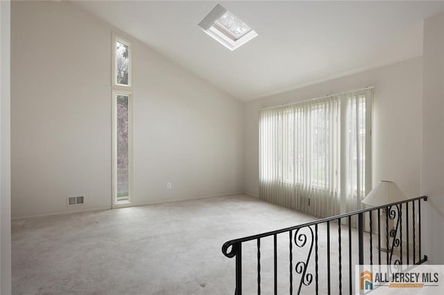 unfurnished room featuring vaulted ceiling with skylight, carpet flooring, baseboards, and visible vents