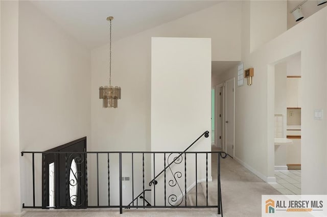 corridor with carpet floors, baseboards, high vaulted ceiling, a chandelier, and an upstairs landing