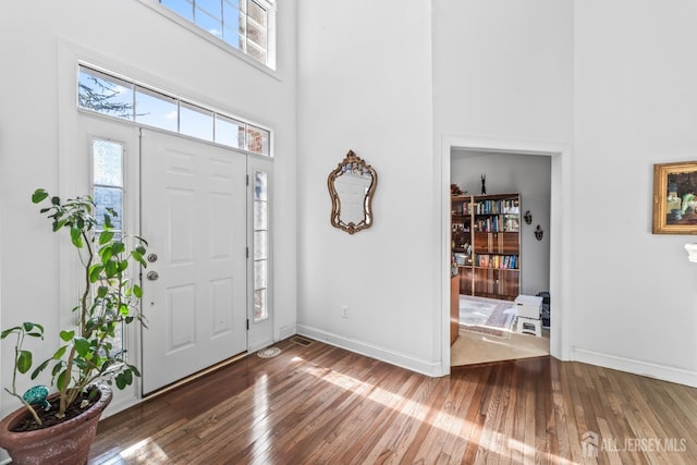 entrance foyer with wood-type flooring, baseboards, and a high ceiling