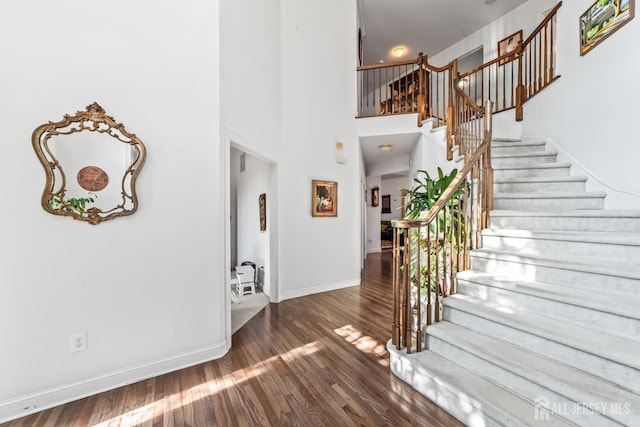 foyer entrance featuring stairs, wood finished floors, a towering ceiling, and baseboards