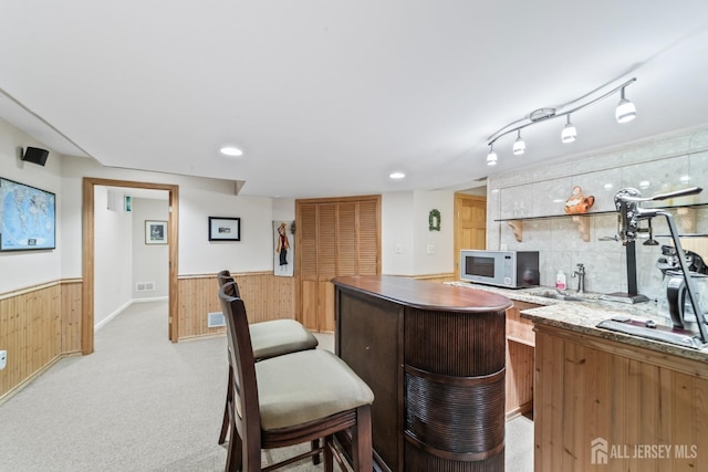 kitchen featuring a center island, light colored carpet, white microwave, wainscoting, and wooden walls