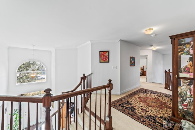 hallway with light colored carpet, an upstairs landing, baseboards, ornamental molding, and an inviting chandelier