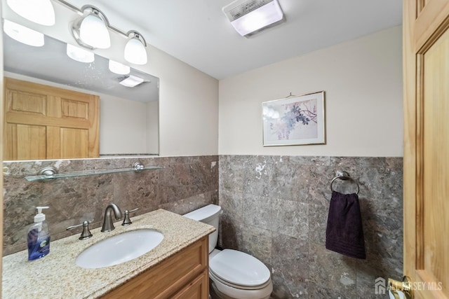 bathroom with a wainscoted wall, tile walls, visible vents, toilet, and vanity