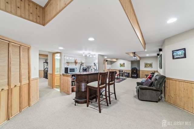 kitchen with white microwave, a wainscoted wall, light carpet, wood walls, and open floor plan