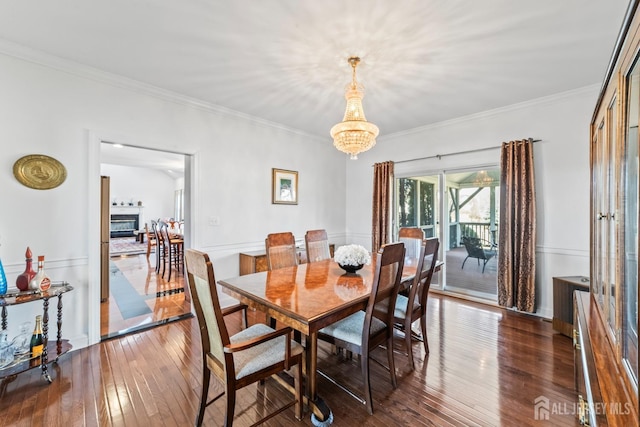 dining area with a notable chandelier, crown molding, hardwood / wood-style floors, and a glass covered fireplace