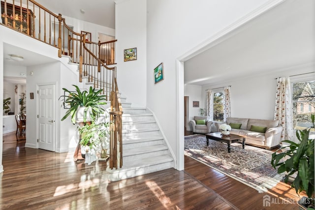 foyer with stairs, wood finished floors, a towering ceiling, and baseboards