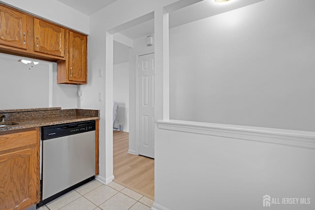 kitchen with brown cabinets, light tile patterned floors, dark countertops, a sink, and dishwasher