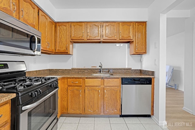 kitchen with stainless steel appliances, brown cabinetry, a sink, and light tile patterned flooring