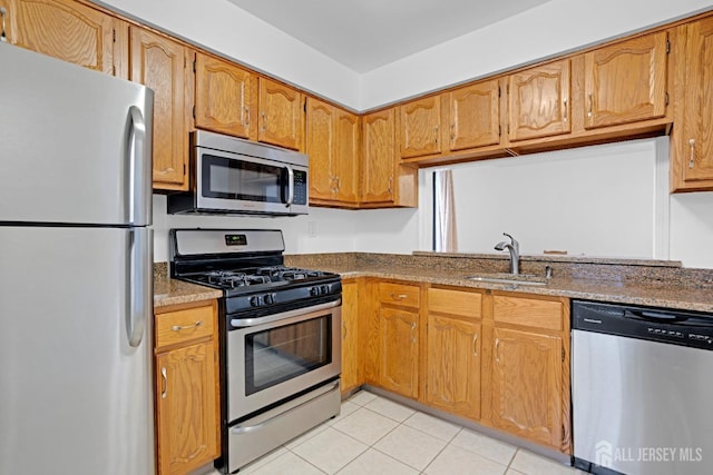 kitchen with stainless steel appliances, brown cabinets, light tile patterned flooring, and a sink