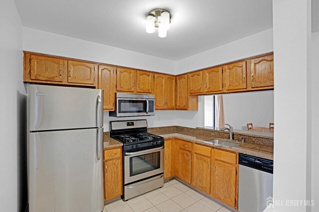 kitchen with light tile patterned floors, appliances with stainless steel finishes, brown cabinets, and a sink