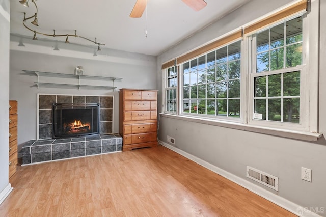 unfurnished living room featuring visible vents, a ceiling fan, wood finished floors, a tile fireplace, and baseboards