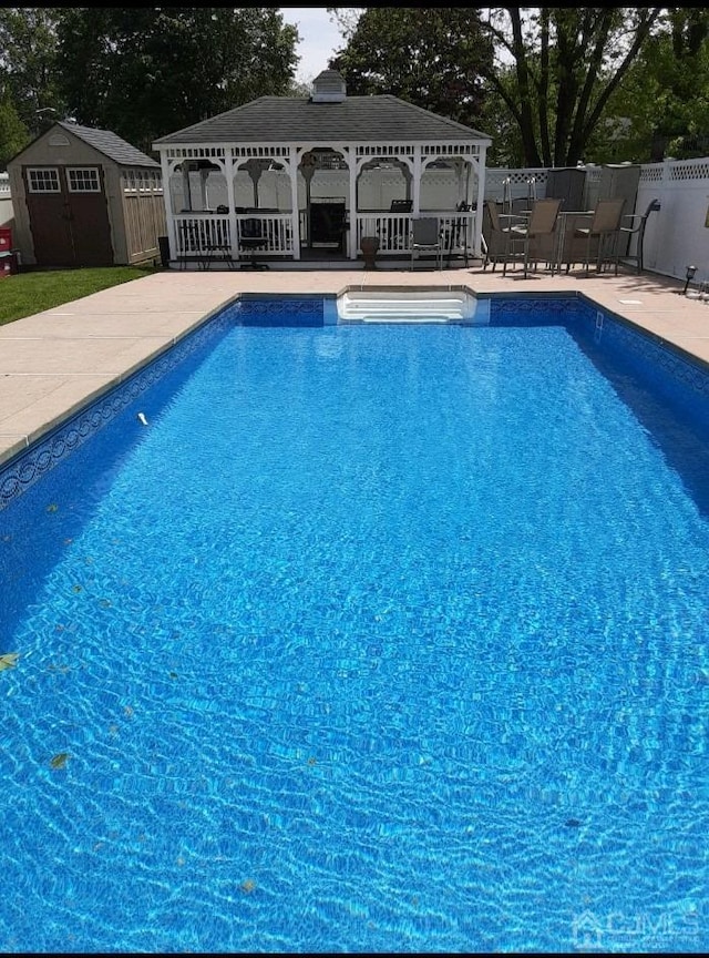 view of swimming pool with an outbuilding, a patio, fence, a gazebo, and a shed