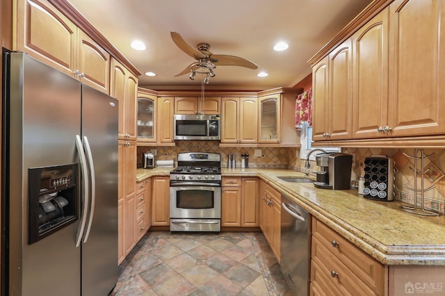 kitchen with tasteful backsplash, light stone counters, glass insert cabinets, stainless steel appliances, and a sink