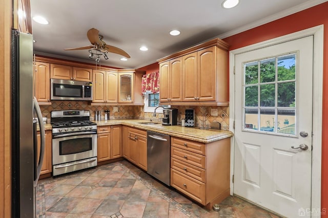 kitchen with light stone counters, crown molding, stainless steel appliances, backsplash, and a sink