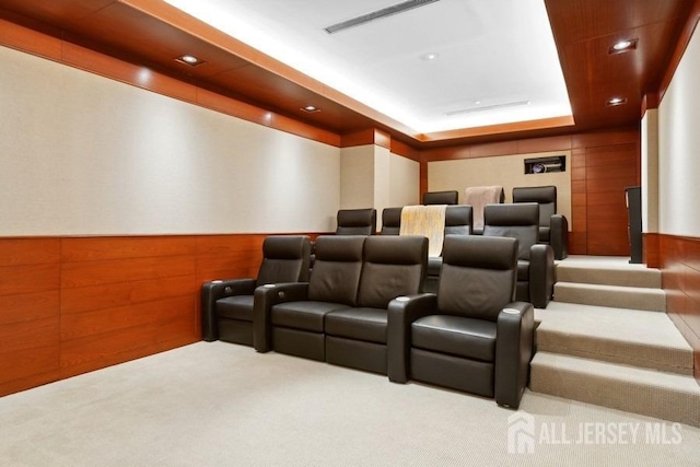 cinema featuring wood walls, a tray ceiling, and light colored carpet