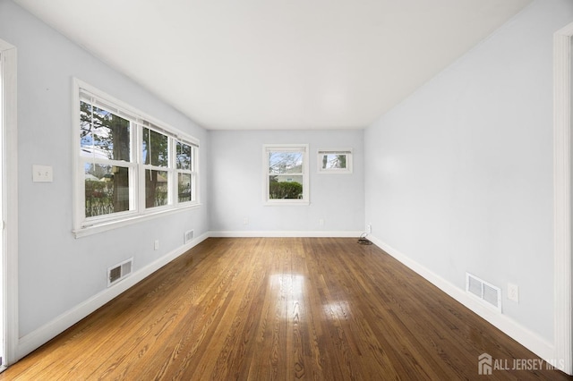 empty room with wood finished floors, a wealth of natural light, baseboards, and visible vents