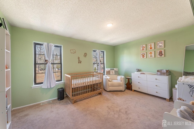 bedroom featuring a crib, carpet flooring, visible vents, and a textured ceiling