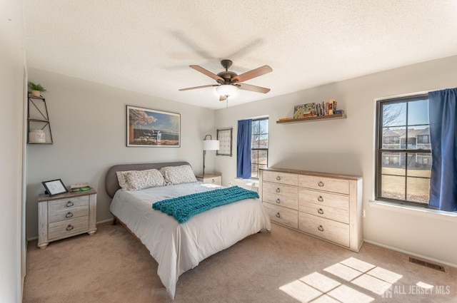 bedroom featuring visible vents, light carpet, a textured ceiling, and ceiling fan