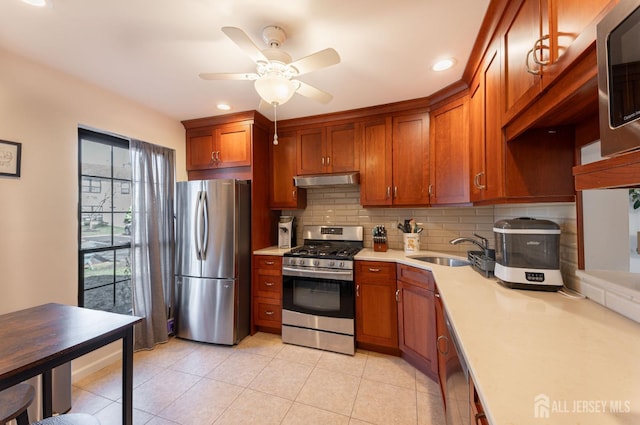 kitchen with tasteful backsplash, under cabinet range hood, light countertops, stainless steel appliances, and a sink