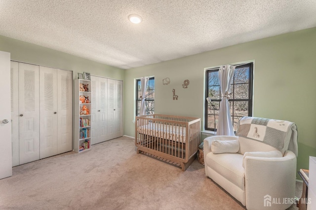 bedroom featuring carpet, multiple closets, and a textured ceiling